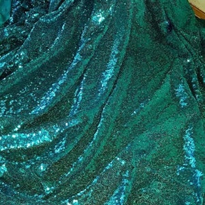 Könnte beinhalten: Tealgrüner Stoff mit Pailletten. Der Stoff ist gefaltet und über eine Oberfläche gelegt.