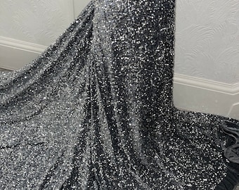 May include: A gray velvet fabric with silver sequins. The fabric has a slight sheen and is perfect for evening wear.