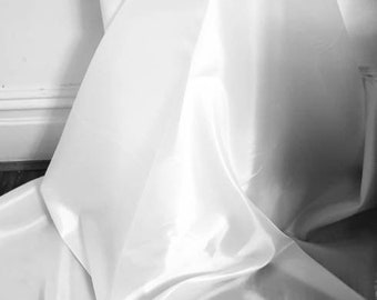 May include: White fabric draped and folded in a soft, flowing manner. The fabric is smooth and has a subtle sheen.