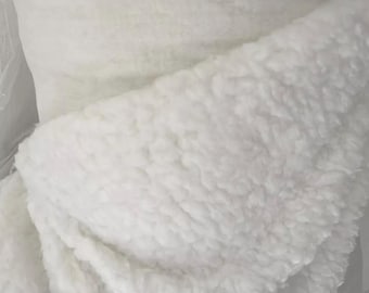 以下が含まれることがあります： 柔らかくふわふわの質感の白いフェイクファー生地。生地は半分に折り畳まれており、素材の内側と外側が示されています。