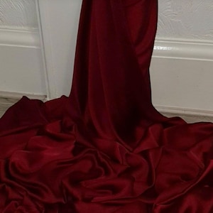 May include: A deep red satin fabric with a smooth, silky texture. The fabric is draped and folded, showcasing its luxurious feel.
