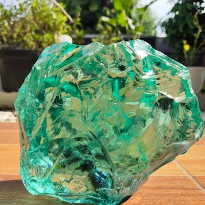 May include: A large, green, glass rock with a rough, textured surface. The rock is translucent and has a light green hue.