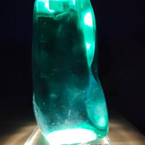 Può includere: Una grande scultura in vetro verde liscio con un'etichetta che dice "498". La scultura è appoggiata su una base in acrilico trasparente.