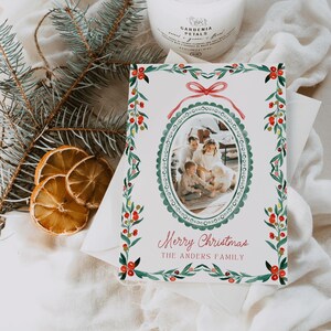 May include: A Christmas card with a family photo inside an oval frame, surrounded by a green and red watercolor design. The card reads "Merry Christmas" and "The Anders Family" in red script. The card is on a white envelope.