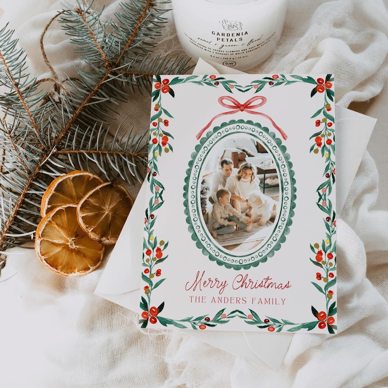 May include: A Christmas card with a family photo inside an oval frame, surrounded by a green and red watercolor design. The card reads "Merry Christmas" and "The Anders Family" in red script. The card is on a white envelope.