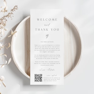 May include: A white card with the words "WELCOME and THANK YOU" in elegant black script, with a heart symbol. The card includes a message and a QR code, resting on a light wooden plate, with dried floral accents.