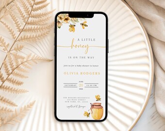 Könnte beinhalten: Ein Smartphone zeigt eine Babyparty-Einladung mit einem Bienen- und Honig-Thema. Der Text lautet "A Little Honey Is On The Way" mit Details für Olivias Rodgers' Party am 21. Juni. Das Design umfasst Aquarellbienen und einen Honigtopf.