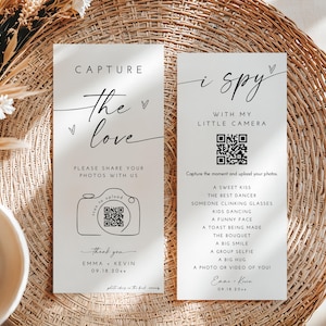 May include: Two white cards with black text on a woven background. One card reads "Capture the love" and includes a camera graphic and a QR code. The other card says "i spy with my little camera" and lists photo prompts.