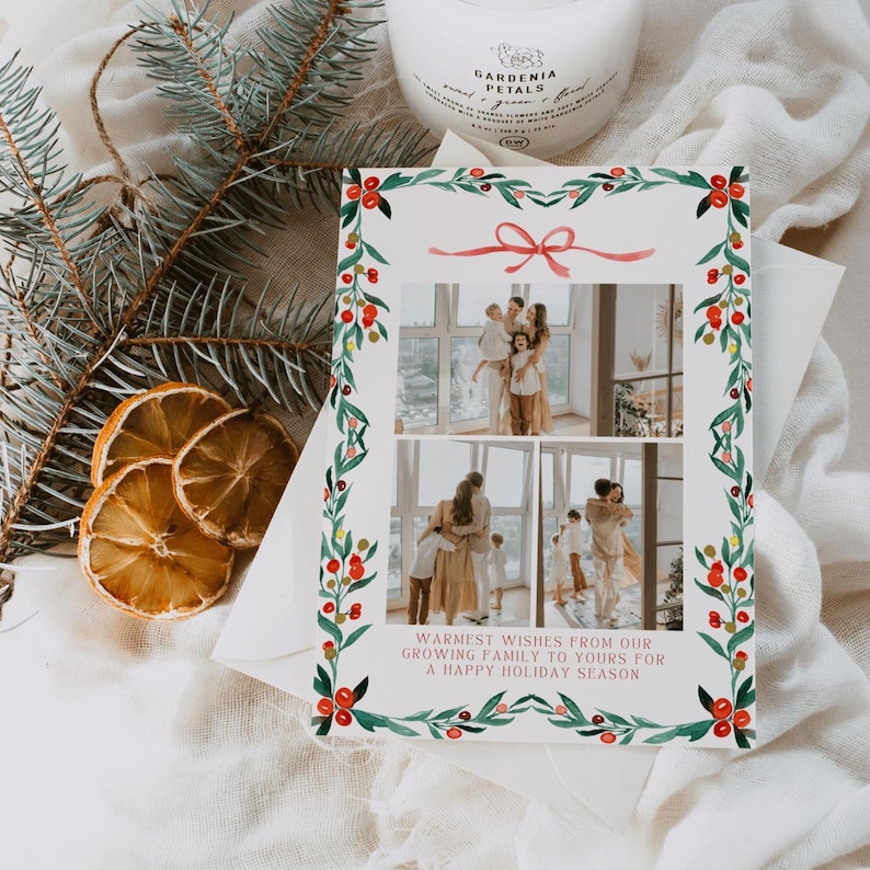 May include: Holiday greeting card with family photos, adorned with a watercolor wreath of green leaves and red berries. The card features a pink ribbon and the text: "Warmest wishes from our growing family to yours for a happy holiday season."