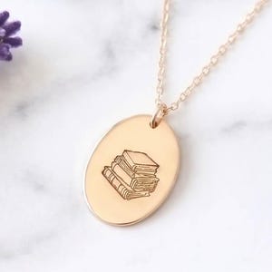 gold filled necklace inscribed with a stack of books surrounded by lavender on a marble surface