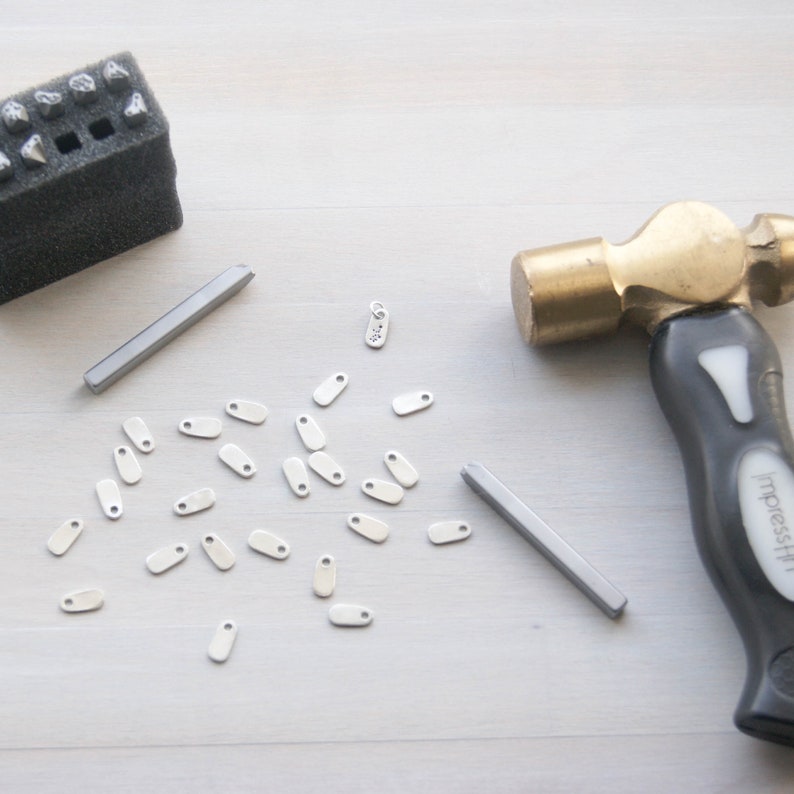 Puede incluir: Un conjunto de suministros para la elaboraci&oacute;n de joyas de metal que incluye un martillo, dos barras de metal, un sello de metal y una colecci&oacute;n de peque&ntilde;os encantos ovalados de metal.