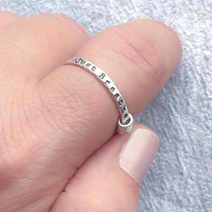 Pu&ograve; includere: Un anello d'argento con le parole "Just Breathe" stampate attorno alla fascia. L'anello &egrave; su un dito e il design include un piccolo dettaglio a spirale nella parte inferiore.