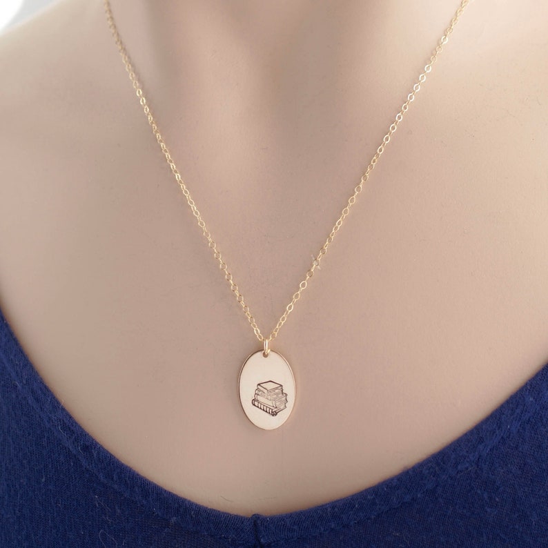 Gold oval necklace stamped with a stack of books on neck