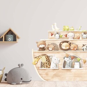 May include: A brown wooden ark with a variety of animals peeking out of the windows. The ark is decorated with colourful flags and a green snake. The ark is on a white wall with a shelf above it.