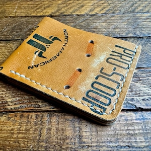 May include: A tan leather wallet with white stitching and the text "PRO-SCOOP" and "NORTH AMERICAN" printed on it.