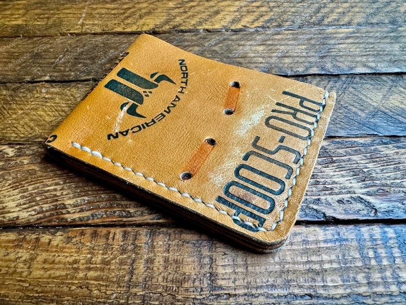 May include: A tan leather wallet with white stitching and the text "PRO-SCOOP" and "NORTH AMERICAN" printed on it.