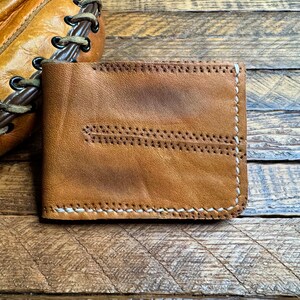 Puede incluir: Una cartera de cuero marr&oacute;n con costuras blancas. La cartera tiene un aspecto desgastado y est&aacute; hecha de cuero de alta calidad.