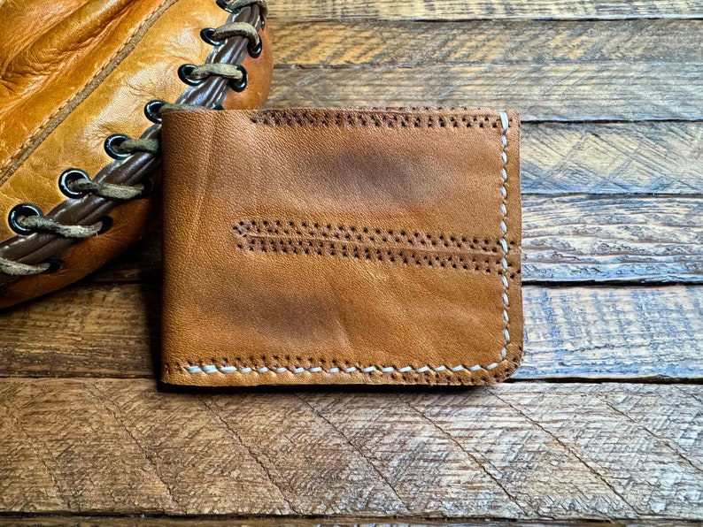 Puede incluir: Una cartera de cuero marr&oacute;n con costuras blancas. La cartera tiene un aspecto desgastado y est&aacute; hecha de cuero de alta calidad.