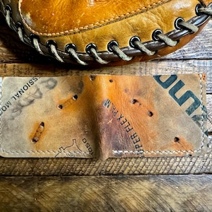Pu&ograve; includere: Un portafoglio in pelle fatto a mano da un guanto da baseball vintage. Presenta cuciture visibili e i segni originali del guanto. Il portafoglio &egrave; marrone e beige, con un aspetto usurato e strutturato.