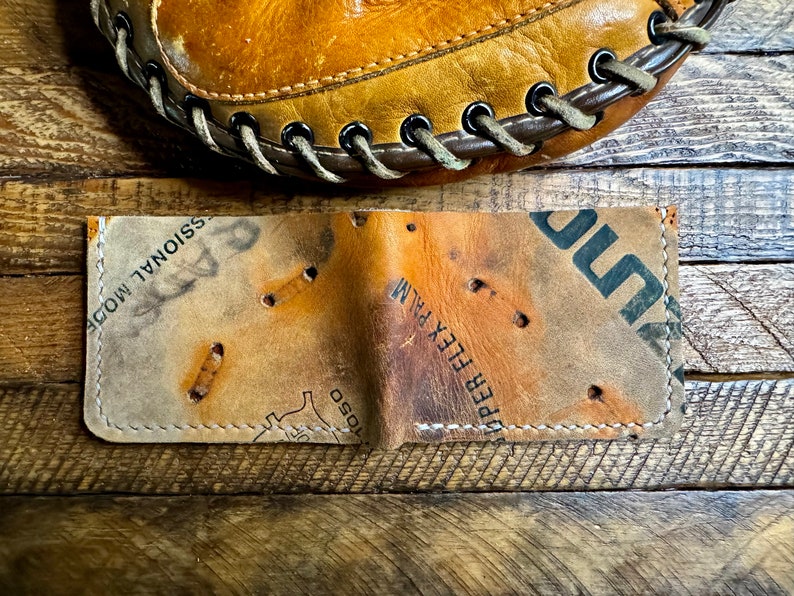 Pu&ograve; includere: Un portafoglio in pelle fatto a mano da un guanto da baseball vintage. Presenta cuciture visibili e i segni originali del guanto. Il portafoglio &egrave; marrone e beige, con un aspetto usurato e strutturato.