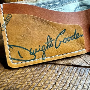 Puede incluir: Una cartera de cuero marr&oacute;n con detalles de costura blanca. La cartera tiene un bolsillo para efectivo y una firma que dice "Dwight Gooden" en tinta verde.