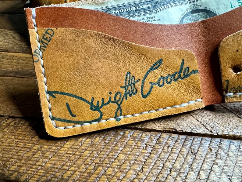 Puede incluir: Una cartera de cuero marr&oacute;n con detalles de costura blanca. La cartera tiene un bolsillo para efectivo y una firma que dice "Dwight Gooden" en tinta verde.