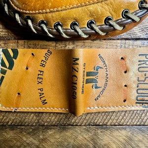 May include: A brown leather baseball glove with white stitching and the text "PRO-SCOOP", "NORTH AMERICAN", "MZ C1050 STEERHIDE", and "SUPER FLEX PALM" printed on it.