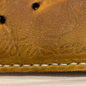 Puede incluir: Primer plano de un guante de b&eacute;isbol de cuero marr&oacute;n con costuras blancas. El guante tiene un logotipo "Wilson" grabado en el cuero.