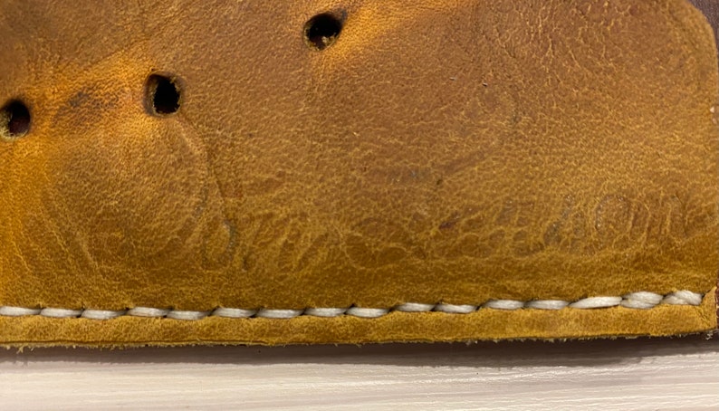 Puede incluir: Primer plano de un guante de b&eacute;isbol de cuero marr&oacute;n con costuras blancas. El guante tiene un logotipo "Wilson" grabado en el cuero.