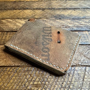 Puede incluir: Una cartera de cuero marr&oacute;n con costuras blancas y la palabra "Dixon" grabada en la parte delantera.