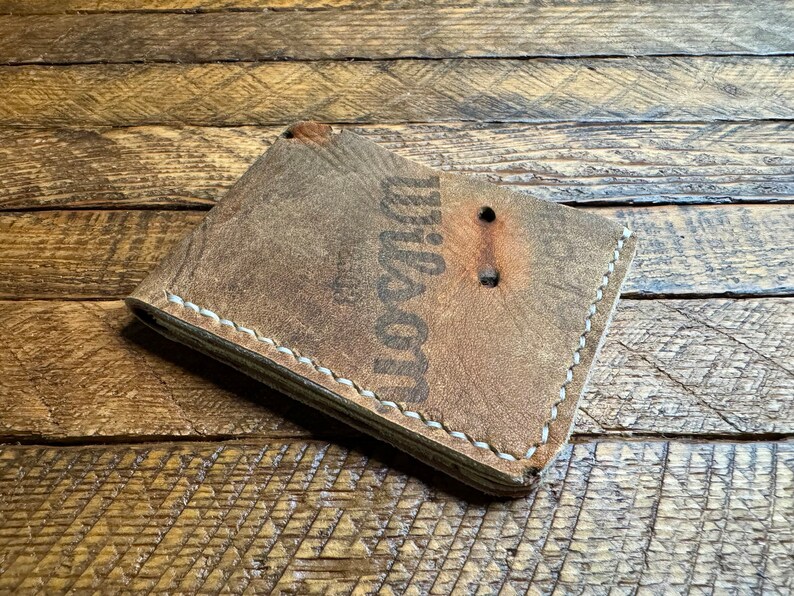 Puede incluir: Una cartera de cuero marr&oacute;n con costuras blancas y la palabra "Dixon" grabada en la parte delantera.