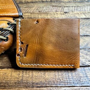 May include: A brown leather wallet with white stitching. The wallet is made of distressed leather and has a rustic look.