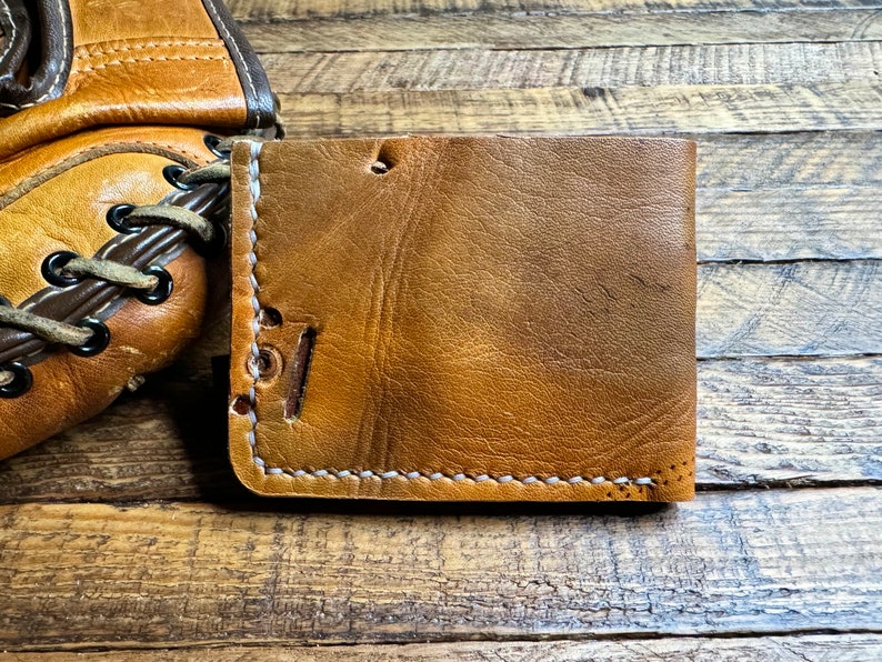 May include: A brown leather wallet with white stitching. The wallet is made of distressed leather and has a rustic look.