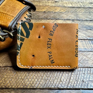 May include: A brown leather wallet with white stitching and the text "Miz Ciuso" and "Super Flex Palm" printed on the front.