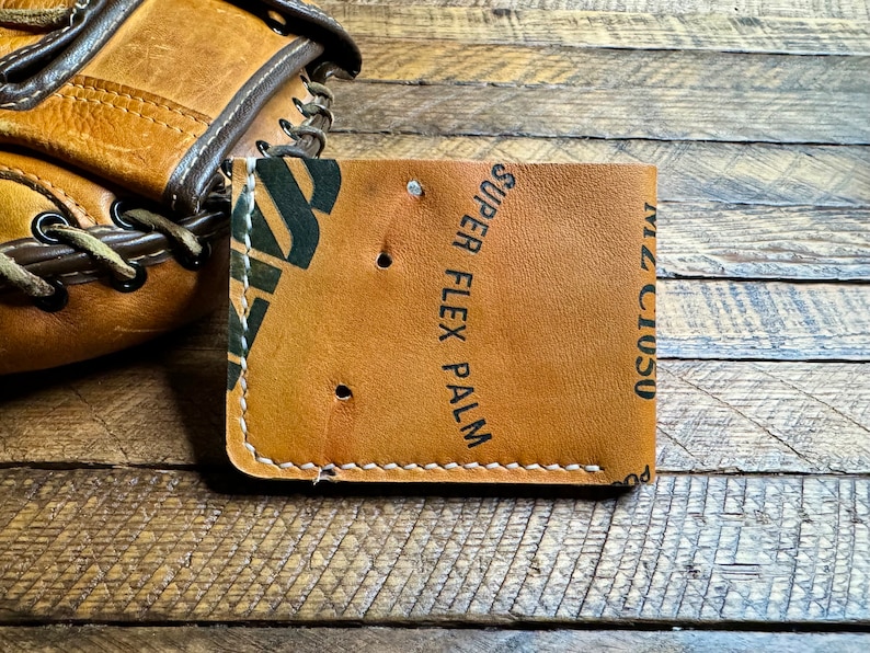 May include: A brown leather wallet with white stitching and the text "Miz Ciuso" and "Super Flex Palm" printed on the front.