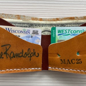 K&ouml;nnte beinhalten: Offene Ledergeldb&ouml;rse in Braun- und Beiget&ouml;nen mit wei&szlig;en N&auml;hten. Die Geldb&ouml;rse enth&auml;lt Bargeld, einen F&uuml;hrerschein aus Wisconsin und eine Westconsin Credit Debitkarte. Die Namen "Willie Randolph" und "MAC 25" sind handschriftlich auf der Geldb&ouml;rse.