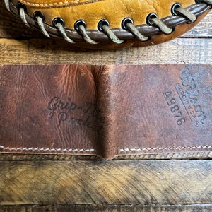 May include: A brown leather wallet with the text "Grip-Tite Pocket" and "Tuf-Nuff Made in U.S.A. 49876" embossed on the front.