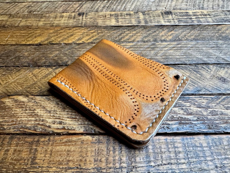May include: A brown leather wallet with white stitching and a distressed look. The wallet has a flap closure and multiple card slots.