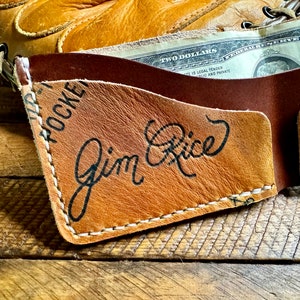 Puede incluir: Una cartera de cuero marr&oacute;n con un borde cosido y el texto "HOCKEY" y "Jim Rice" en letras negras.