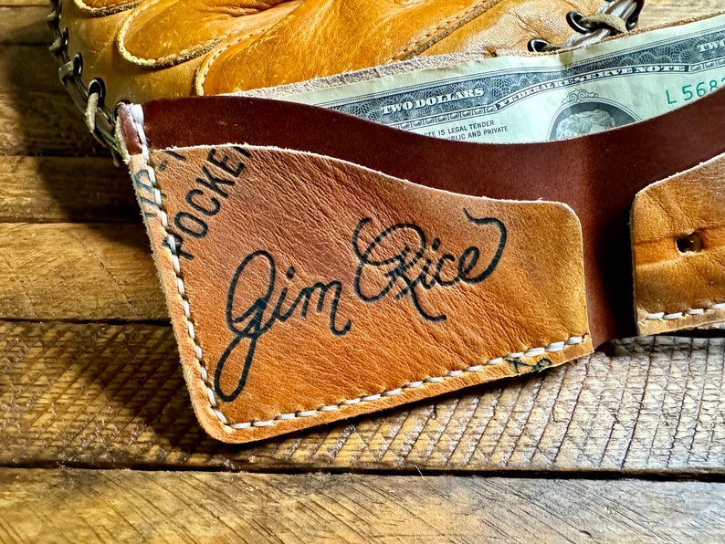 Puede incluir: Una cartera de cuero marr&oacute;n con un borde cosido y el texto "HOCKEY" y "Jim Rice" en letras negras.