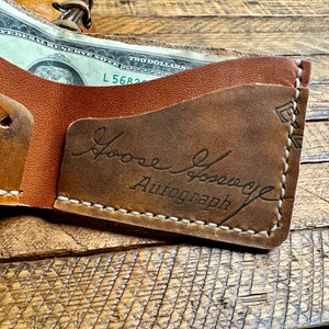 May include: A brown leather wallet with a white stitch detail. The wallet is open and has a billfold and a card slot. The inside of the wallet has a brown leather patch with the text "Loose Groove Autograph" embossed in black.
