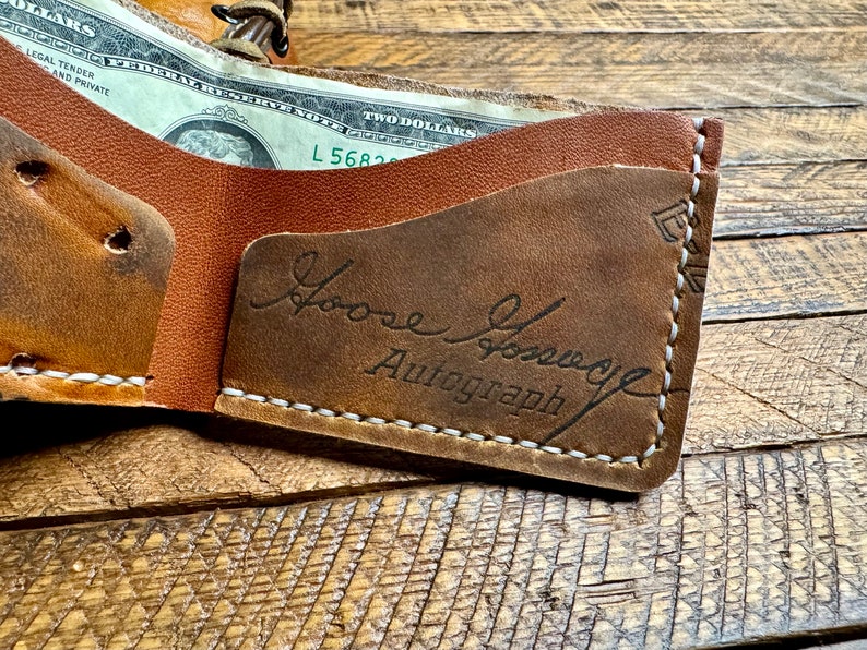 May include: A brown leather wallet with a white stitch detail. The wallet is open and has a billfold and a card slot. The inside of the wallet has a brown leather patch with the text "Loose Groove Autograph" embossed in black.