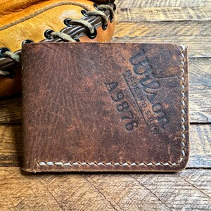 May include: A brown leather wallet with the text "Wilson Made in USA" and the number "A9876" embossed on the front.
