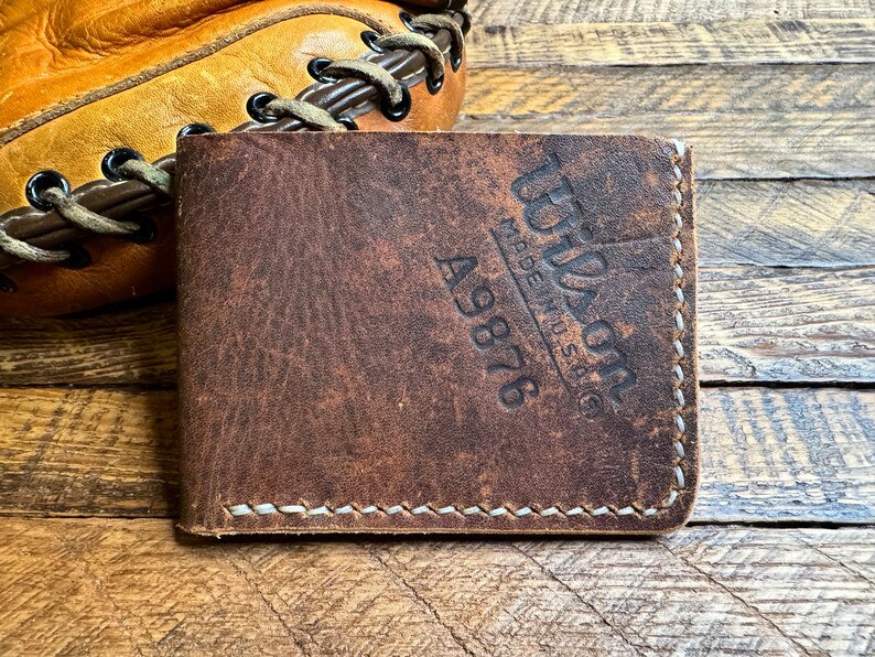 May include: A brown leather wallet with the text "Wilson Made in USA" and the number "A9876" embossed on the front.