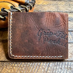 May include: A brown leather wallet with white stitching and the text "Grip-Fit Pocket" embossed on the front.