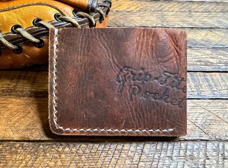 May include: A brown leather wallet with white stitching and the text "Grip-Fit Pocket" embossed on the front.