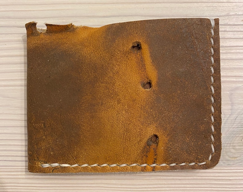 Puede incluir: Una cartera de cuero marr&oacute;n con costuras blancas y tres agujeros en la parte delantera. La cartera est&aacute; desgastada y tiene un aspecto desgastado.