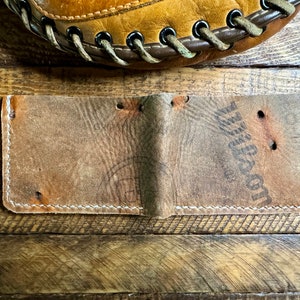 Puede incluir: Una cartera de cuero marr&oacute;n con costuras blancas y la palabra "Wilson" grabada en la parte delantera.