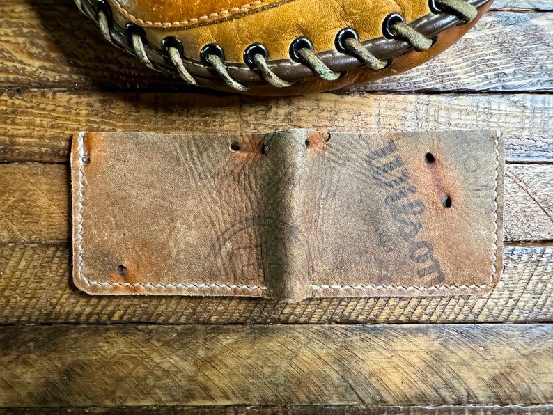 Puede incluir: Una cartera de cuero marr&oacute;n con costuras blancas y la palabra "Wilson" grabada en la parte delantera.