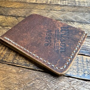 May include: A brown leather wallet with white stitching and the text "Wilson Made in U.S.A.&reg; A9876" embossed on the front.
